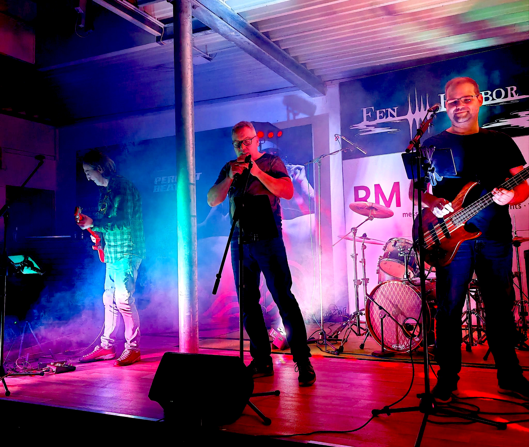 Ein Foto während des Auftritts - es sind ein Gitarrist, ein Sänger und ein Bassist zu sehen, der Schlagzeuger im Hintergrund ist nicht zu erkennen.
