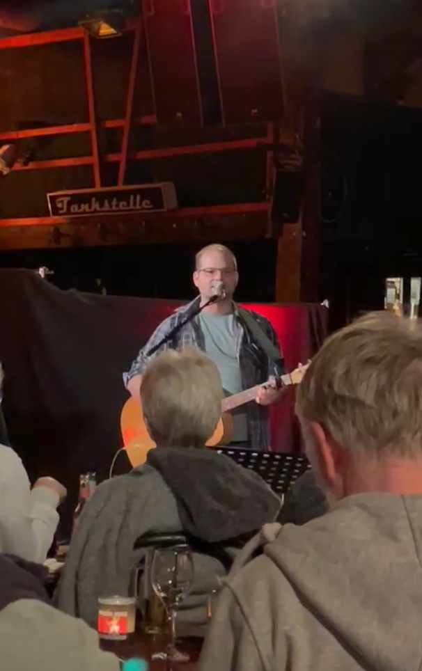 Ein Foto von mir, aus dem Publikum aufgenommen. Man sieht einige Hinterköpfe von Menschen aus dem Publikum