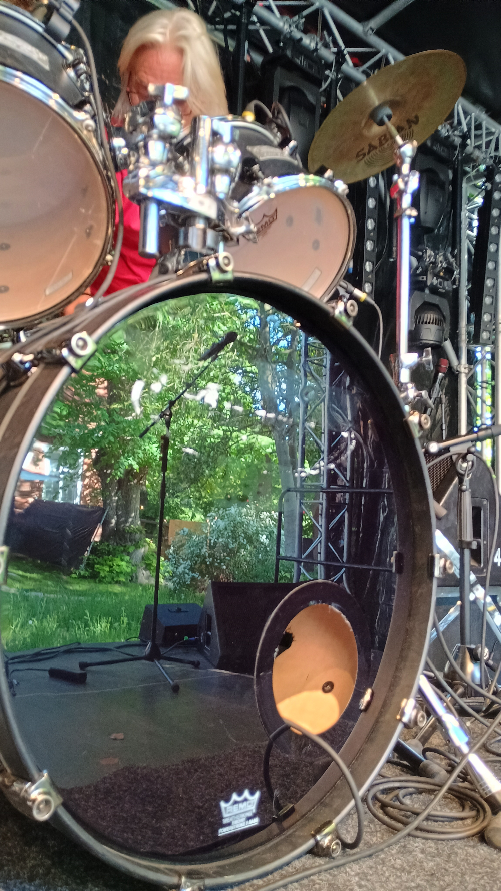 Ein Foto der Bühne beim Aufbau. Man sieht das Schlagzeug von vorne. In der Bassdrum spiegelt sich der Platz vor der Bühne.