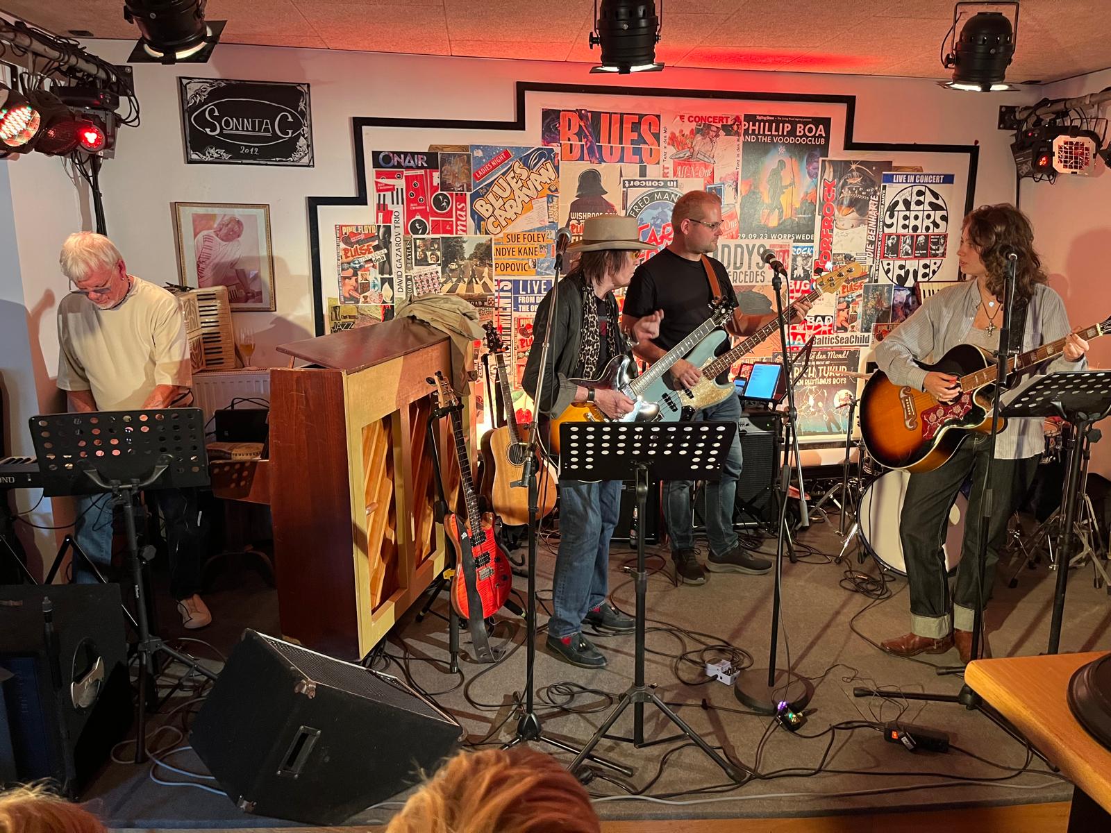 Ein Foto von der Bühne an dem Abend. Zu sehen sind Blue Weaver am Piano, Brian Parrish an der Gitarre, Carsten Pfeffer am Bass und "Emily" mit Gitarre und Gesang (der Schlagzeuger ist nicht zu sehen)